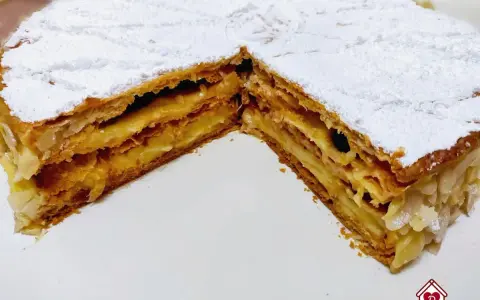 Un delizioso millefoglie alla crema, con strati croccanti di pasta sfoglia e una ricca crema pasticcera, spolverato di zucchero a velo e mandorle.