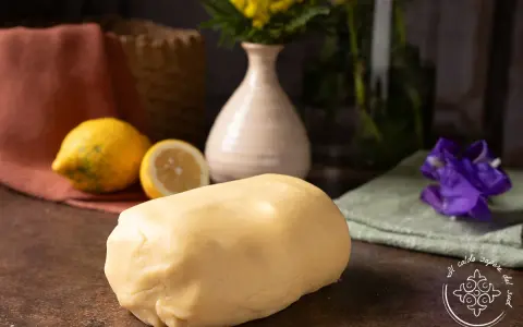 Impasto di pasta frolla che non si rompe, pronto per creare dolci perfetti. Accanto, limoni freschi e un tocco di colore.