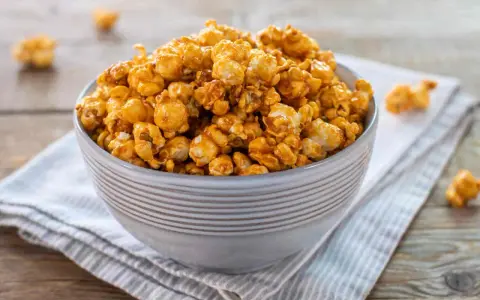 Una ciotola piena di pop corn caramellati, dorati e invitanti, su un tovagliolo a righe.