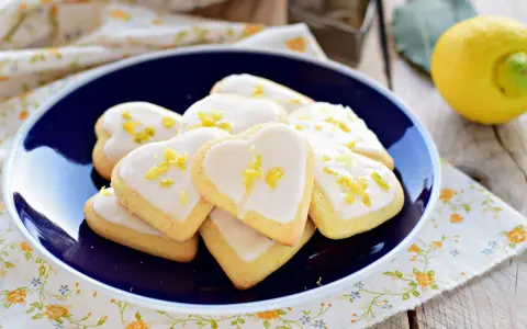 Cuore di biscotti al limone glassati, decorati con scorza di limone, su un piatto blu.