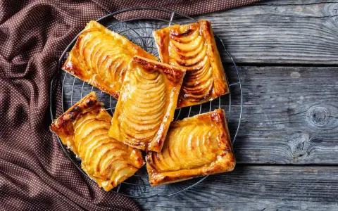 Sfogliatine di pasta sfoglia con zucchero e mele, dorate e lucide, su una griglia di raffreddamento.