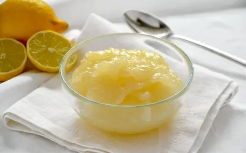 Una ciotola di deliziosa crema al limone senza uova, con limoni freschi affettati sullo sfondo.