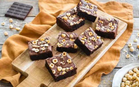 Deliziosi brownie senza glutine con nocciole tostate su tagliere di legno.
