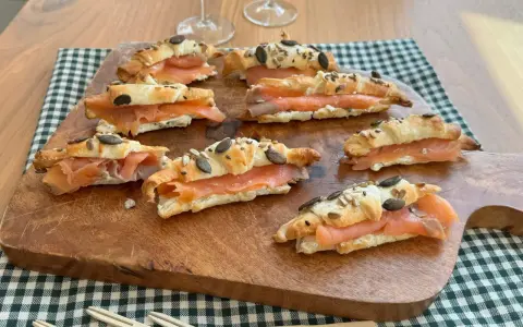 Cornetti di pasta sfoglia ripieni di salmone affumicato e formaggio cremoso, guarniti con semi.