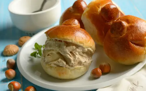 Brioches col tuppo, soffici e dorate, ripiene di gelato cremoso. Un dolce siciliano da gustare con nocciole e menta.