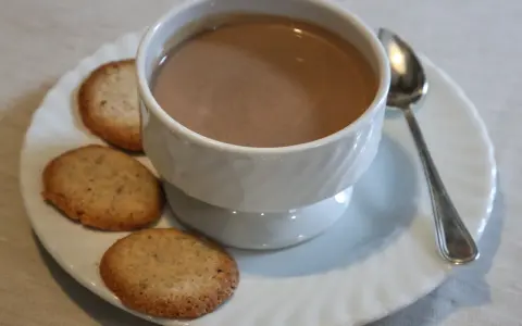 Tazza di crema di cogne fumante con biscotti secchi su un piattino bianco, accompagnata da un cucchiaino.