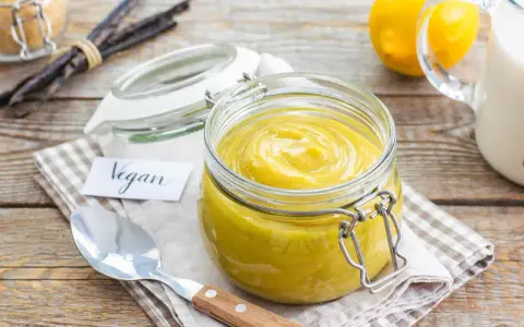Crema pasticcera vegana in un barattolo di vetro, con bacche di vaniglia e limoni sullo sfondo.