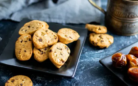 Biscotti vegan con gocce di cioccolato e datteri su piatti neri, pronti per una pausa golosa.