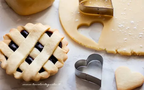 Una crostata con ripieno di marmellata, pasta frolla stesa e tagliabiscotti a forma di cuore.
