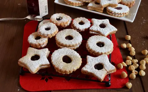 Deliziosi biscotti Linzer, a forma di stella e tondi, ripieni di marmellata e spolverati di zucchero a velo, su una griglia nera.