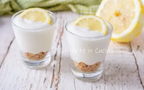 Due bicchierini di mousse al limone con base croccante e fetta di limone, su un tavolo di legno.