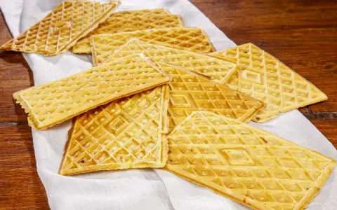 Un mucchio di croccanti ferratelle abruzzesi, dolci tradizionali, disposte su un panno bianco su un tavolo di legno.