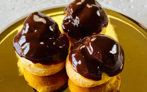 Tre golosi bignè al cioccolato, lucidi e invitanti, su un piatto dorato.