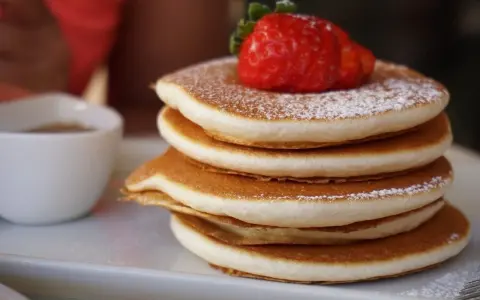 Pancake Bimby perfetti, impilati e spolverati di zucchero a velo, con una fragola fresca in cima.