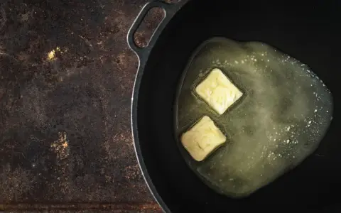 Due cubetti di burro a pomata si sciolgono in una padella, pronti per creare una base saporita.