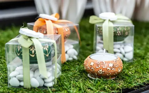 Confezioni regalo con confetti bianchi, candela e decorazioni floreali. Il significato dei confetti, augurio di dolcezza e prosperità.