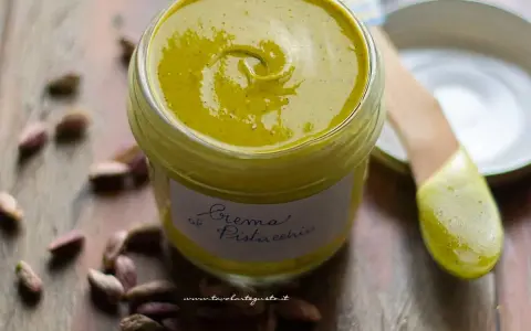 Vasetto di crema di pistacchio fatta in casa, con pistacchi sparsi intorno. La ricetta perfetta per una delizia!