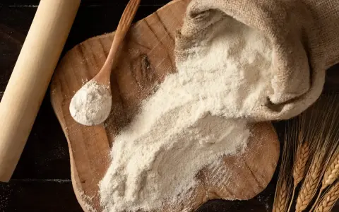 Farina 0 al posto della 00 nei dolci: un sacco di farina, un mestolo e spighe di grano su un tagliere di legno.
