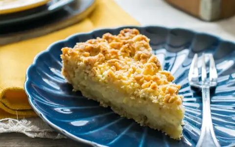 Fetta di sbrisolona con crema pasticcera su piatto blu, con forchetta trasparente.