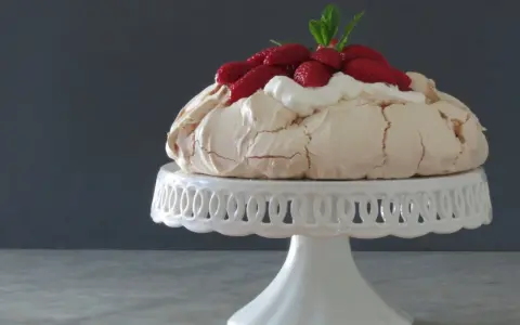 Pavlova ricetta: meringa croccante fuori e morbida dentro, guarnita con panna montata e fragole fresche.
