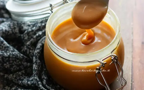 Un cucchiaio raccoglie un denso caramello salato senza panna da un barattolo di vetro.