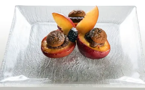 Deliziose pesche ripiene con biscotti e frutti di bosco, un dolce invitante su un piatto di vetro.