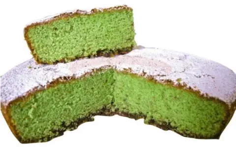 Una fetta di torta alla menta verde brillante, cosparsa di zucchero a velo, è appoggiata su una torta intera.