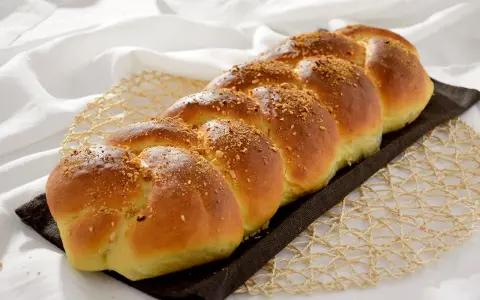 Treccia dorata di dolci con farina manitoba, cosparsa di granella croccante, su un letto di lino bianco.