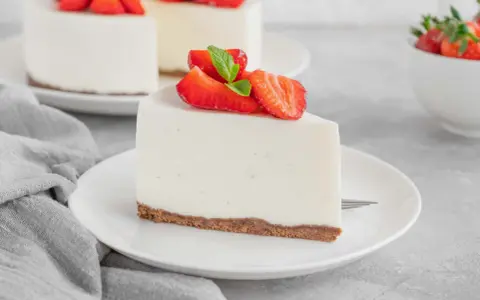 Una fetta di torta fredda allo yogurt senza biscotti, guarnita con fragole fresche e menta, su un piatto bianco.