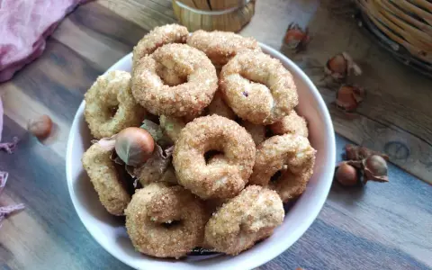 Ciambelline al vino cosparse di zucchero, con nocciole sparse sul tavolo di legno.