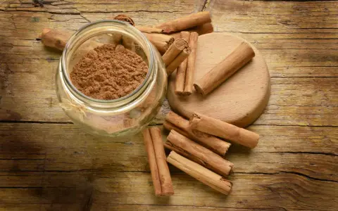 Barattolo di cannella in polvere e bastoncini su un tagliere di legno. Ingredienti essenziali per la cucina.