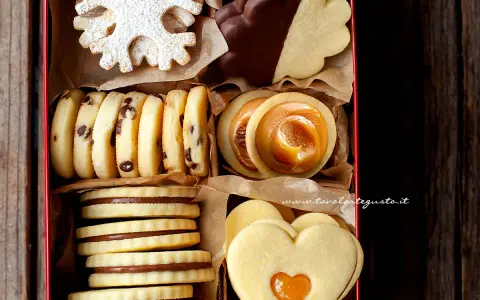 Scatola piena di biscotti al burro: a fiocco di neve, con gocce di cioccolato, ripieni di caramello, a forma di cuore e ricoperti di cioccolato.