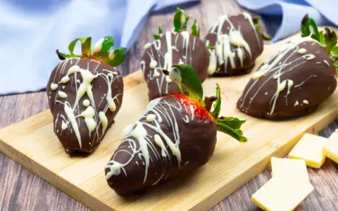 Fragole ricoperte di cioccolato fondente e decorate con cioccolato bianco. Un delizioso assaggio di frutta al cioccolato su un tagliere di legno.