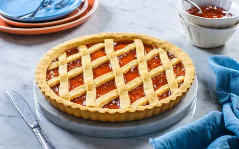 Crostata alla marmellata dorata, perfetta per il tempo cottura crostata forno statico. Servita su un piatto di marmo con tovagliolo blu.