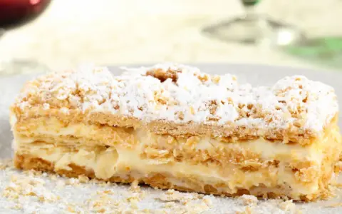 Una fetta di rettangolare torta millefoglie compleanno, con crema pasticcera e zucchero a velo.