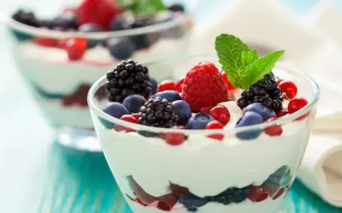Deliziosa mousse allo yogurt con frutti di bosco freschi e una fogliolina di menta, servita in coppette di vetro.