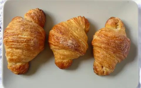 Tre deliziosi croissant dorati, cosparsi di zucchero, disposti su un piatto grigio.