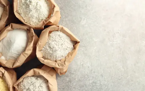 Sacchetti di carta aperti pieni di diverse farine, tra cui farina 0 e manitoba, pronte per creare pane e dolci.