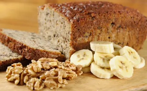 Fetta di banana bread senza uova, con noci e banane a fette, su tagliere di legno.