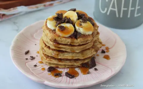 Pancake light con banana, cioccolato e sciroppo d'acero su un piatto rosa.