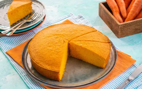 Una deliziosa torta di carote, appena sfornata, è tagliata a fette su un piatto. Accanto, un cesto di carote fresche.