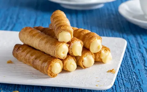 Un mucchio di cannoncini alla crema dorati, ripieni di una crema pasticcera liscia e invitante, pronti per essere gustati.
