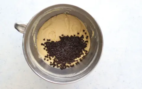 Impasto per torta con abbondanti gocce di cioccolato in una ciotola di metallo, pronto per essere infornato.