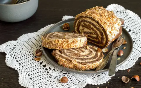 Rotolo alla Nutella ricoperto di granella di nocciole, servito su un piatto con due fette tagliate.