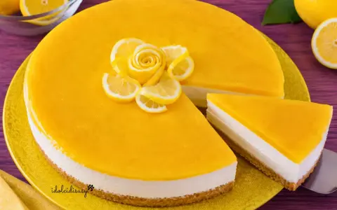 Cheesecake al limone con decorazione di fettine e rosa di limone. Una fetta è già servita.