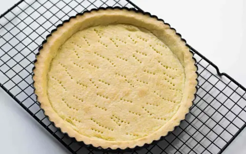 Base di pasta frolla appena sfornata, con fori per la cottura, su una griglia metallica.