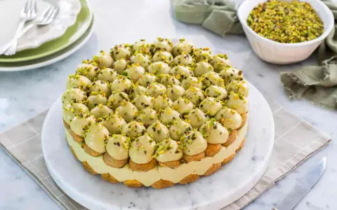 Torta rotonda con tante piccole meringhe verdi, guarnite con granella di pistacchio. Un delizioso tiramisù al pistacchio pronto per essere gustato.