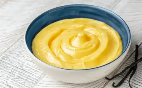 Una ciotola di crema gialla, liscia e invitante, con baccelli di vaniglia accanto. Perfetta per ogni ricetta crema.