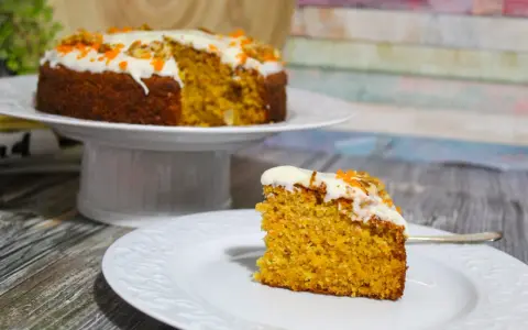 Una fetta di torta di carote senza glutine, soffice e profumata, con glassa bianca e decorazioni arancioni.