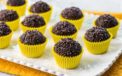 Deliziosi dolcetti brasiliani, brigadeiros al cioccolato, ricoperti di codette, serviti in pirottini gialli su un piatto bianco.
